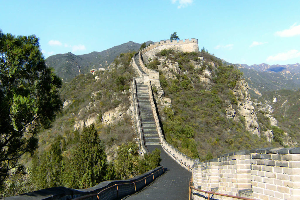 An uphill stretch of the Great Wall of China, visitable from Beijing on a daytrip. Either side is lush green trees and grass