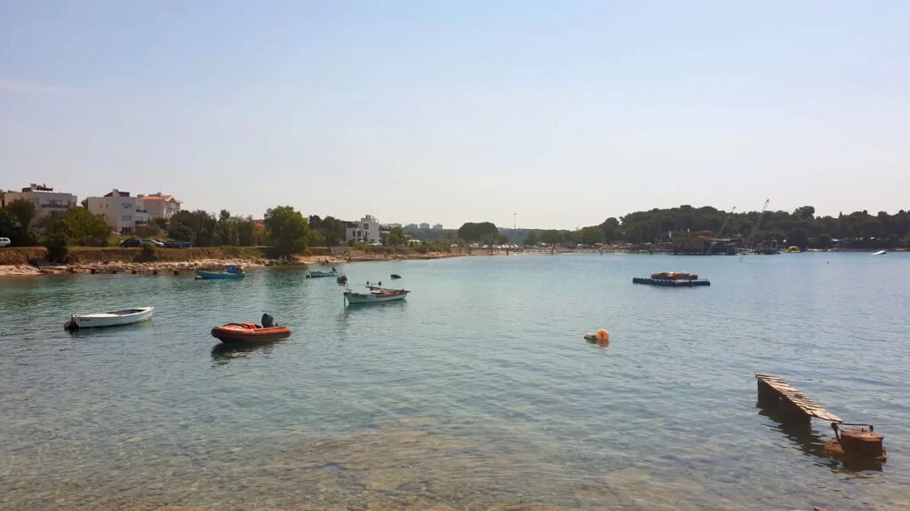 Panoramic shot of Valovine Beach with dingy boats anchored in the shallow, clear waters of the bay.