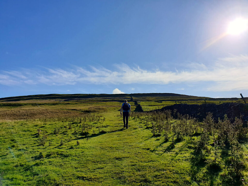 The ascent crosses many fields, the summit is still far in the distance! The sun beams down on the vast green fields.