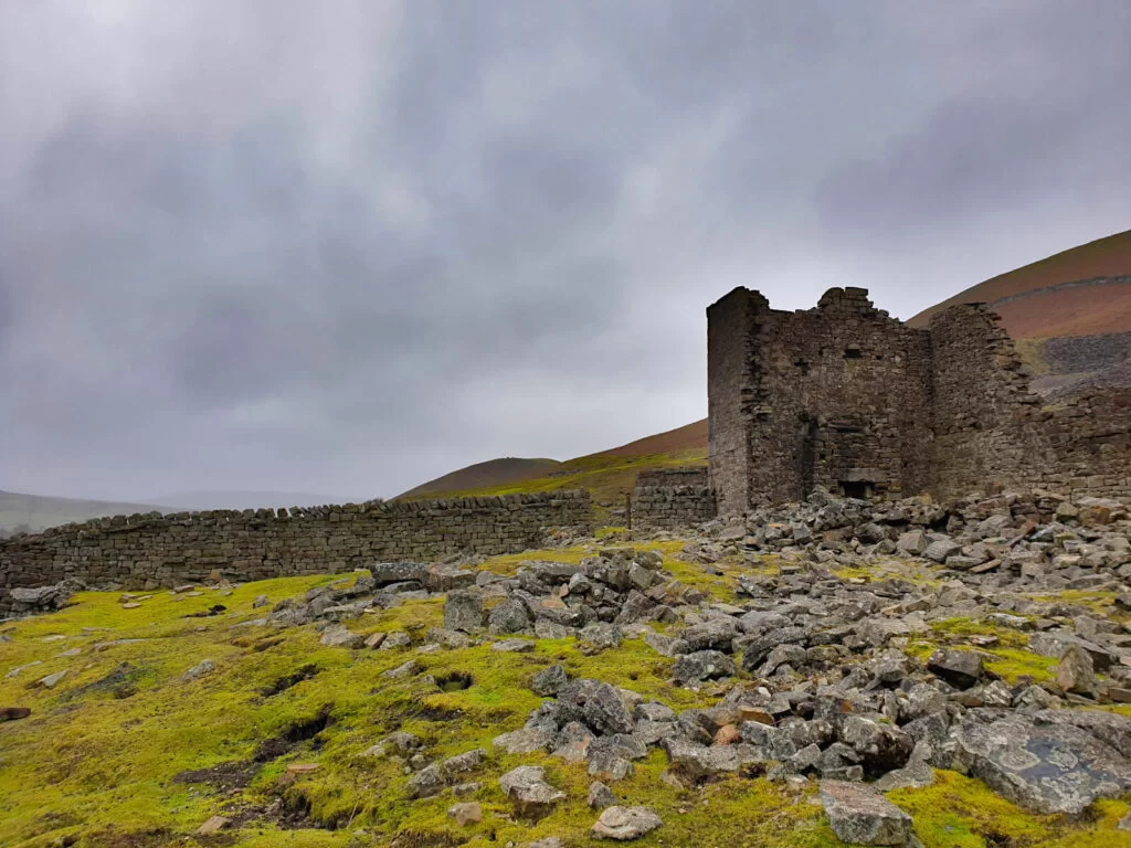 The abandoned grounds of Crackpot Hall stand in contrast to the dark clouds behind, the grass is lush green thanks to the wet weather.
