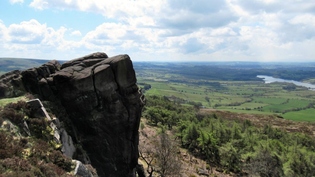 An incredible viewpoint from one the Peak District's best walks, The Roaches. Looking out over the Peak District Countryside from a rocky protrusion with a reservoir in the background.