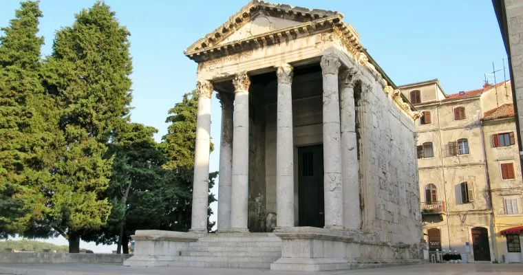 A roman-era temple with stairs leading up to the front four columns with a intricately patterned triangular roof. The building shows signs of it's 2000 year age but is otherwise well-preserved and not crumbling.