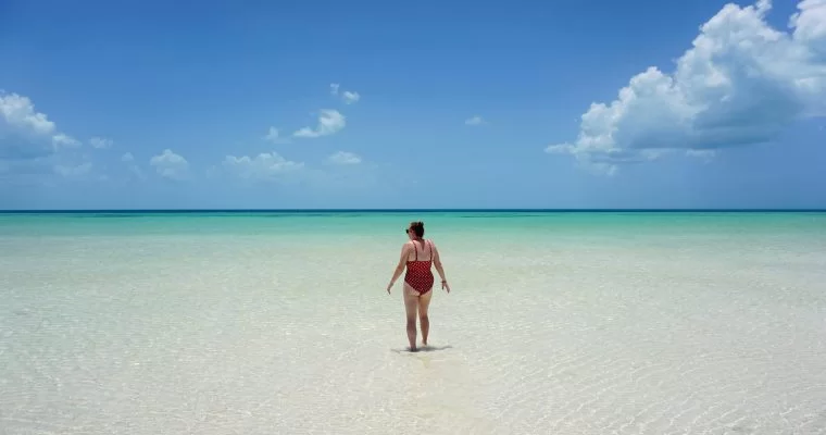 Punta Mosquito in Holbox is postcard paradise. In the image you can see a white sand beach covered by shallow clear water and a perfect blue sky. Zoe is stood in the centre of the image looking out to sea.