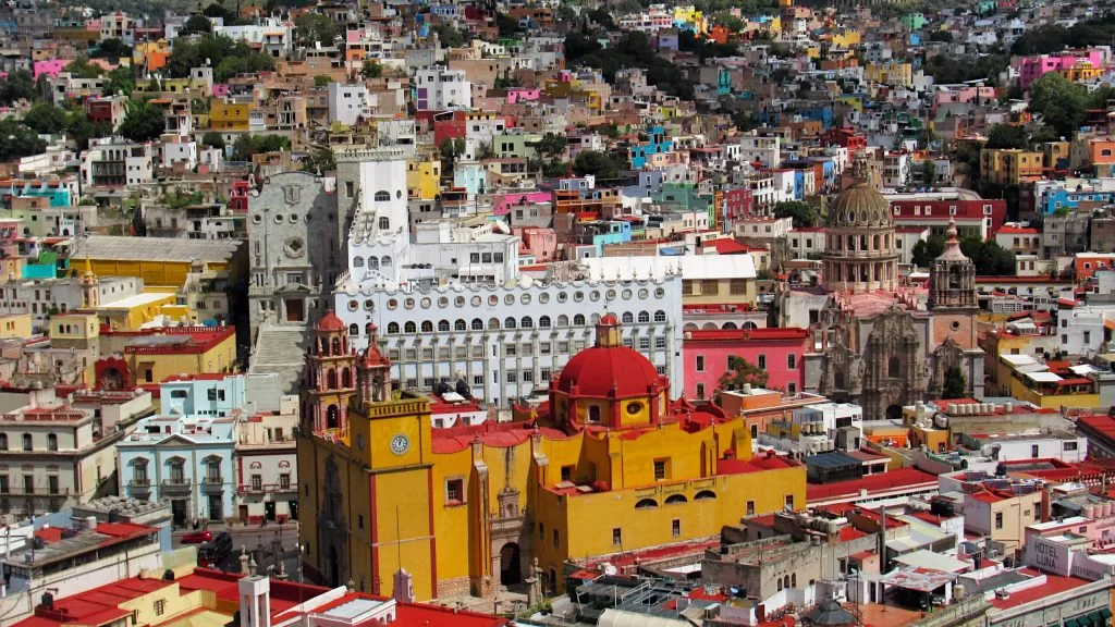 The bright buildings of Guanajuato in the background. Nearest the cameras are the iconic yellow Basilica and the University