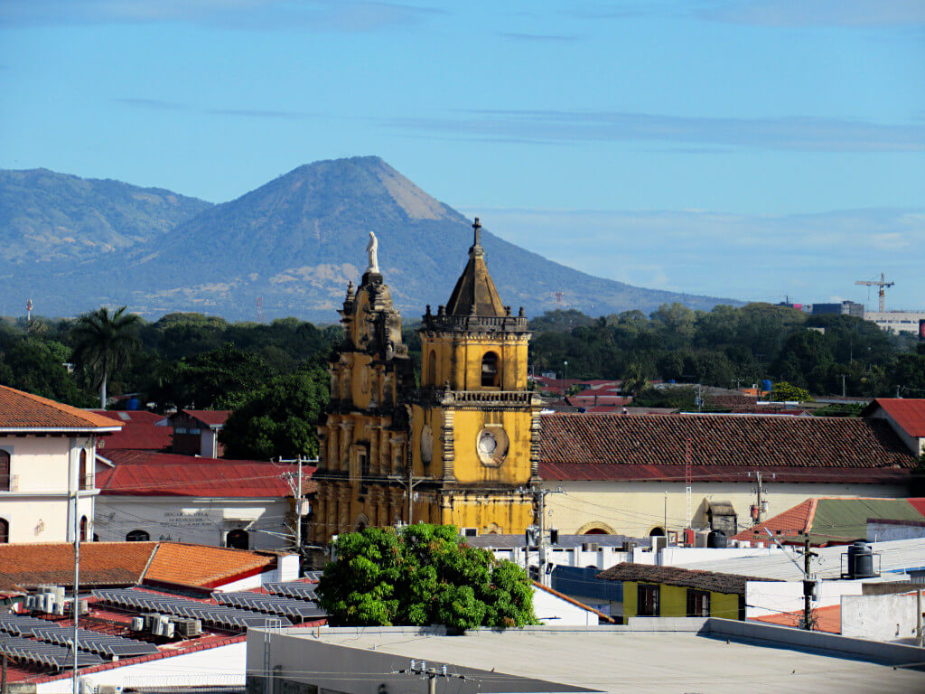A yellow church building with a volcano in the distance behind in Leon Nicaragua