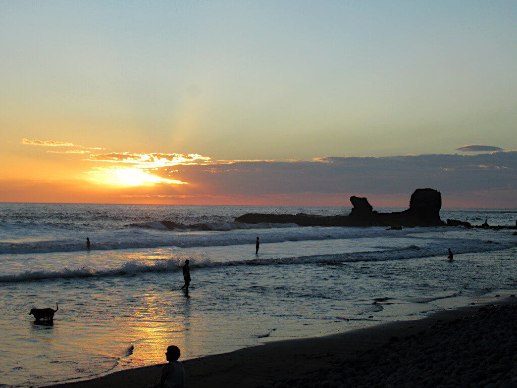 Overlooking the iconic rock formation just off of Playa El Tunco El Salvador. With the sun setting in the background and a few people walking through the shallow waves