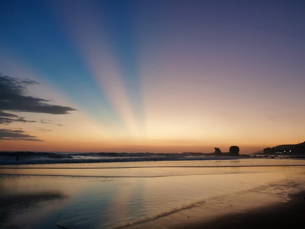 A calm and peaceful sunset over the ocean from Playa El Tunco. The sky is shades of blue, pink, yellow and orange