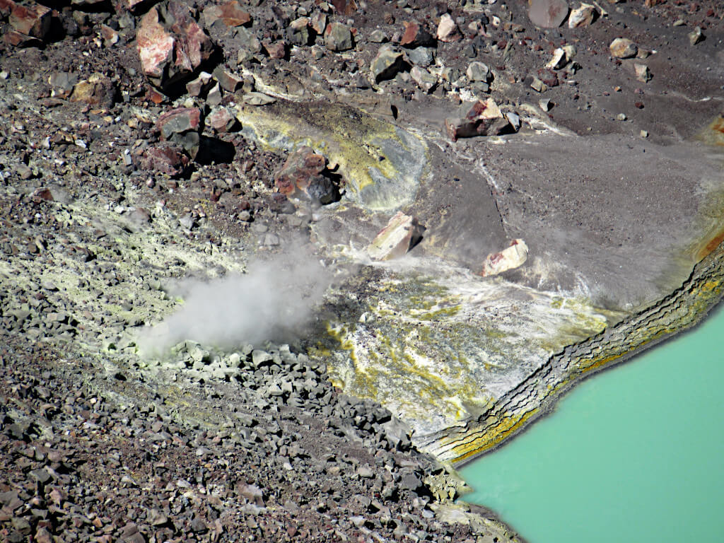 Steam from the volcano as well as loose rock and sulphurous layers around the edge of the lake