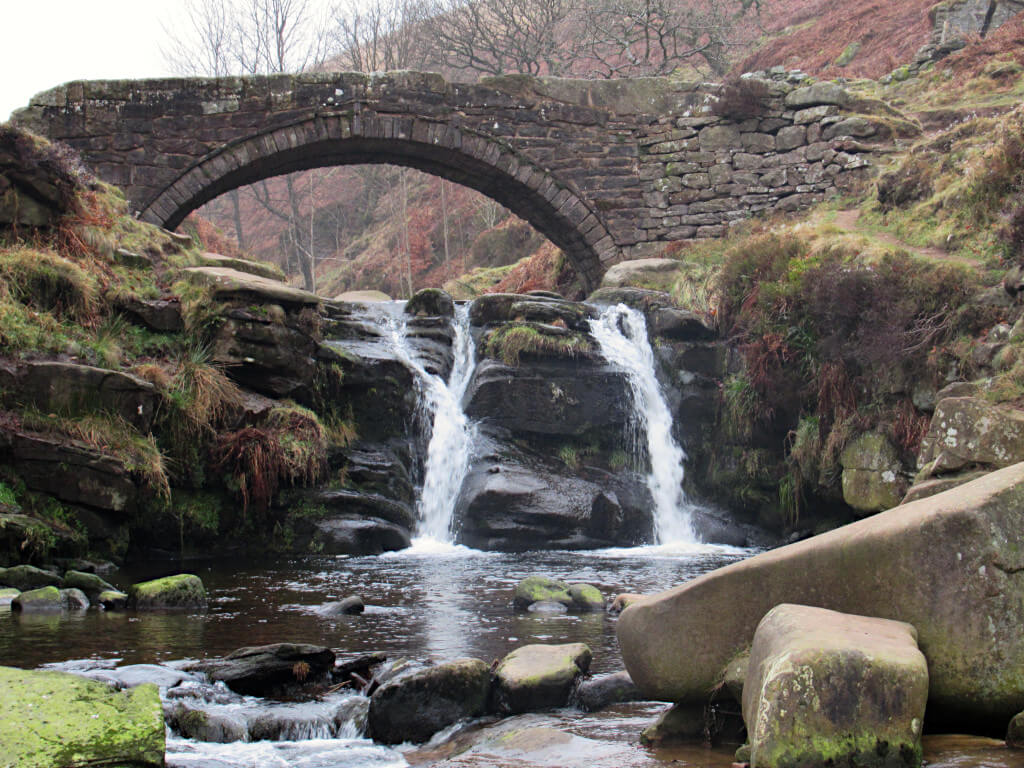 Water flows over the waterfall underneath the 18th century stone bridge at Three Shires Head
