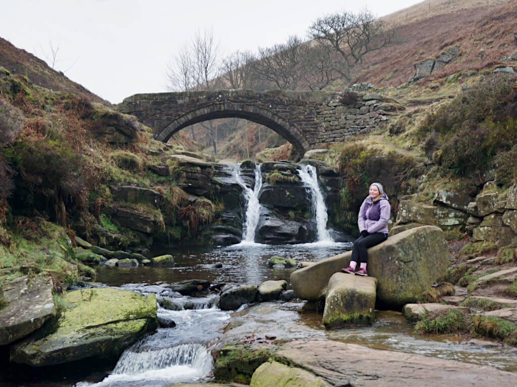 Zoe sits on a rock in front of the largest waterfall at 3 Shires Head