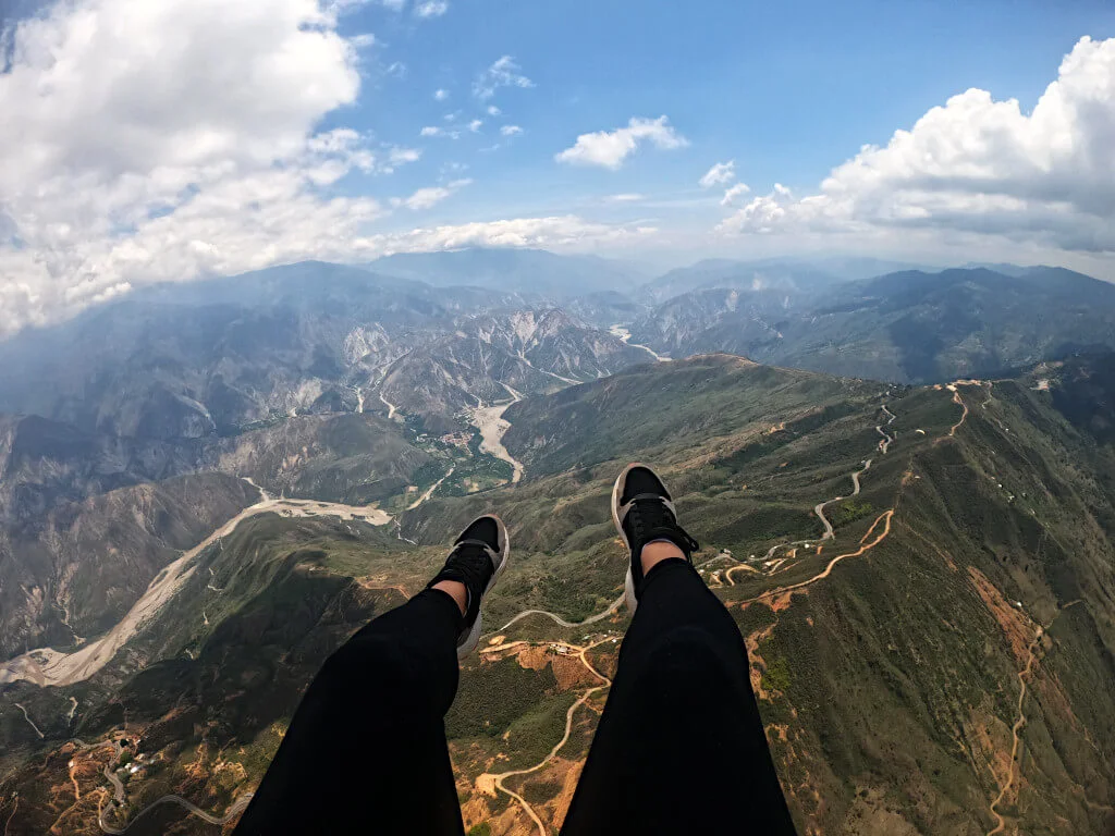 Zoe's legs and feet visible in shot with the canyon and national park below from a mile above the ground while paragliding