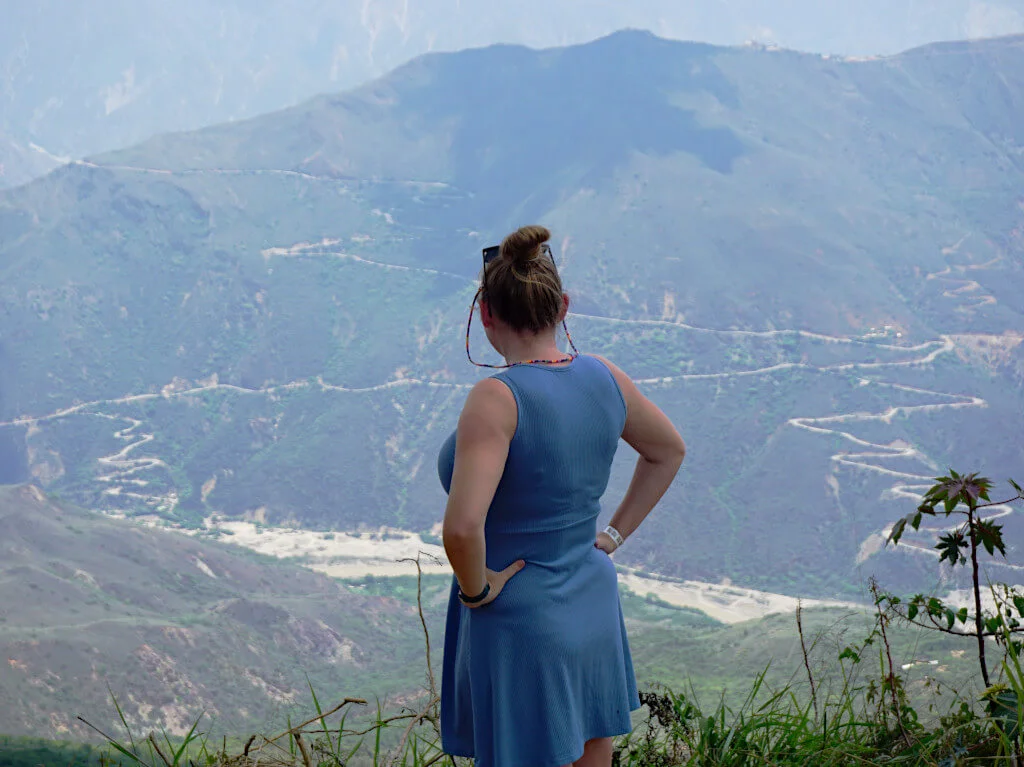 Zoe overlooking the Chicamocha Canyon, facing away from the camera she is wearing a blue dress and her hair in a bun