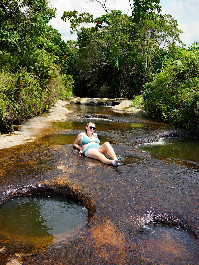 Zoe laying on the river surrounded by the plunge pools, she is wearing a green bikini and sunglasses