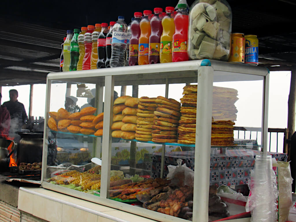 A variety of snacks available from the food stalls, pictured include arepas, empanadas, corn on the cob and sausages. Colourful soft drinks line the top shelf
