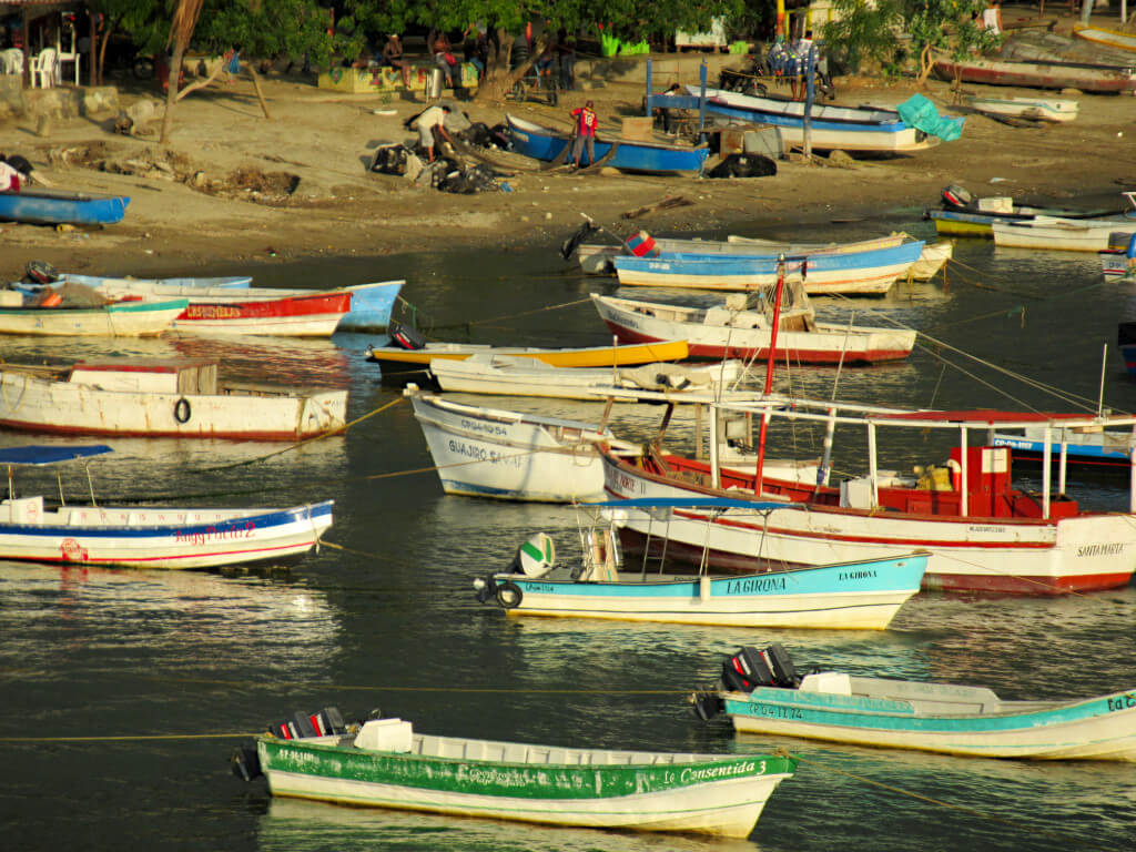 A close-up shot of the boats anchored in the water. Litter is visible on the beach behind