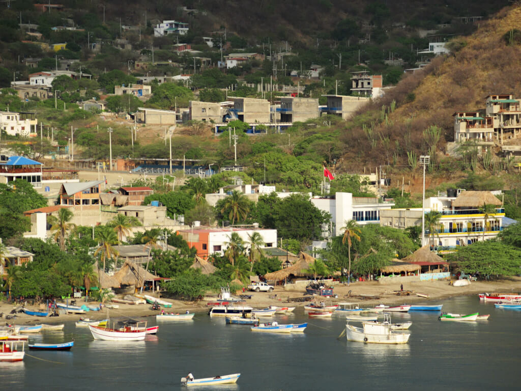 Boats line Taganga Beach both on the shore and in the water, the basic buildings of the town are visible behind the beach