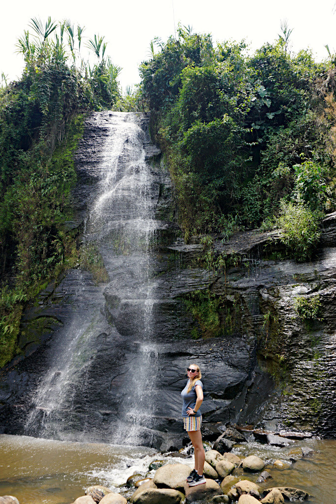 Zoe stood in front of one of the waterfalls at Tres Cascadas. She is wearing a blue t-shirt and striped shorts with her hands on her hips