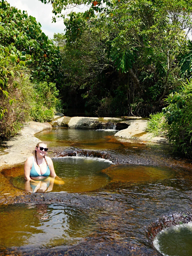 The best thing about Guadalupe Santander is the natural plunge pools at Quebrada Las Gachas. Zoe sits in a shallow pool in the sunshine. She is wearing a green bikini and sunglasses