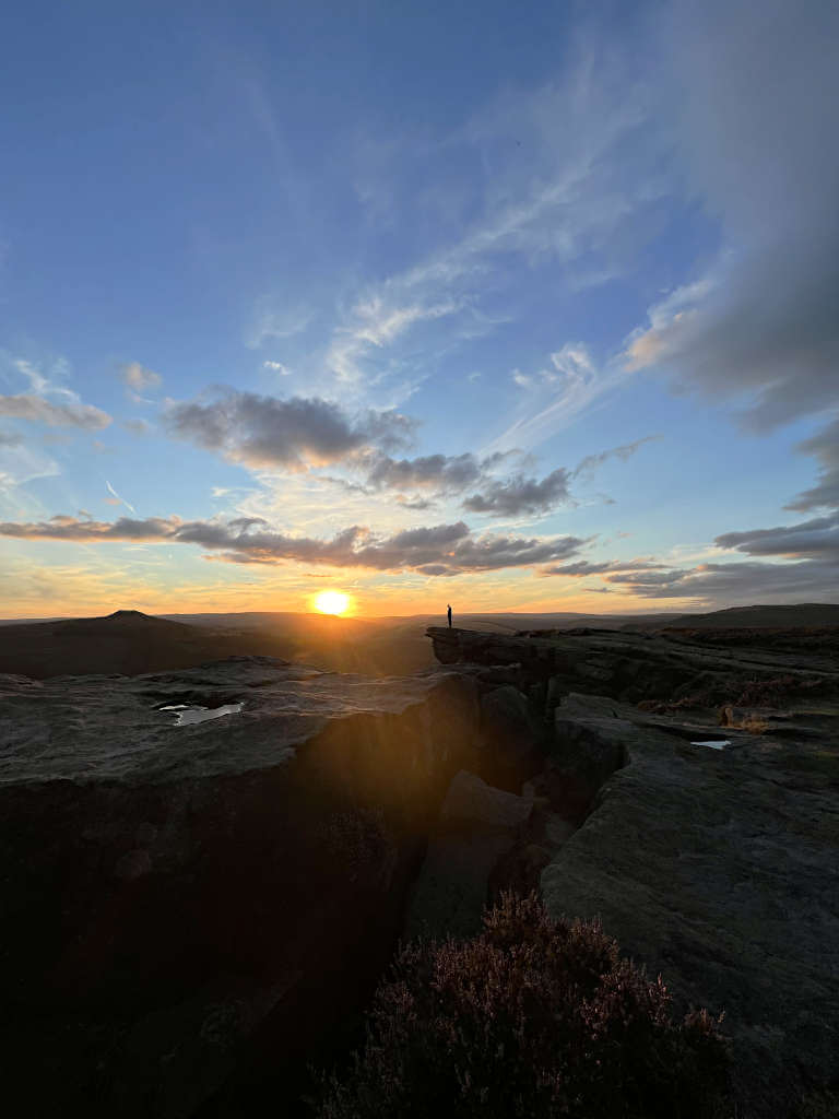 The silhouette of a man standing on the edge of Bamford Rocks at sunset