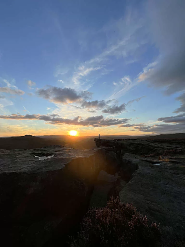 The silhouette of a man standing on the edge of Bamford Rocks at sunset