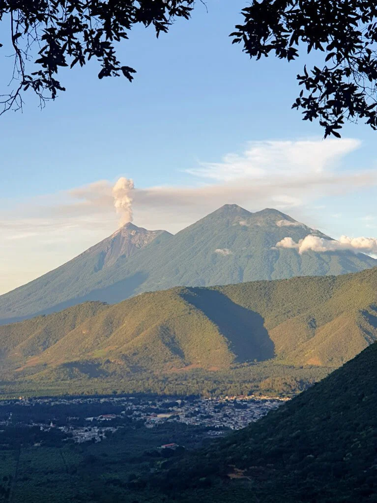 Fuego is erupting, seen from the hills around Antigua Guatemala with Acatenango visible between the clouds. These two are some of the best options for hiking volcanoes in Guatemala, with simply breathtaking experiences.