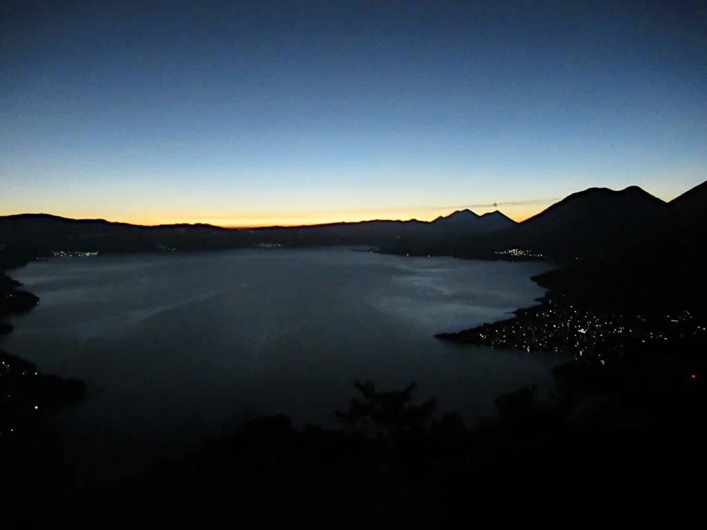 Dawn over Lake Atitlan, a plume of smoke is visible from the crater of Volcan Fuego against the just-yellow sky