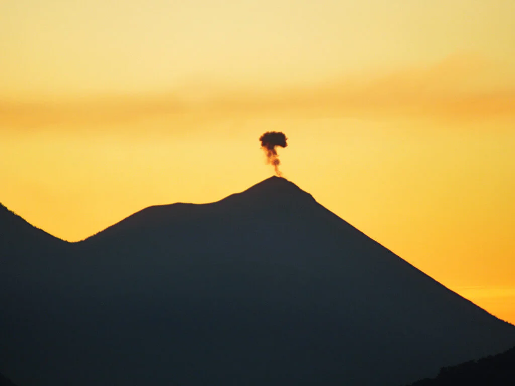 Volcan Fuego erupting at sunrise, the sky is a vivid yellow-orange colour