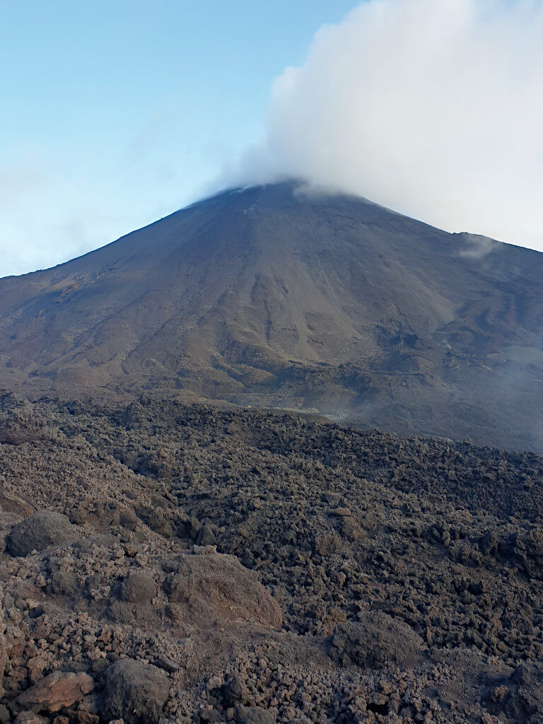 Steam rises from the crater and sides of Pacaya, scorched rock is visible in the foreground