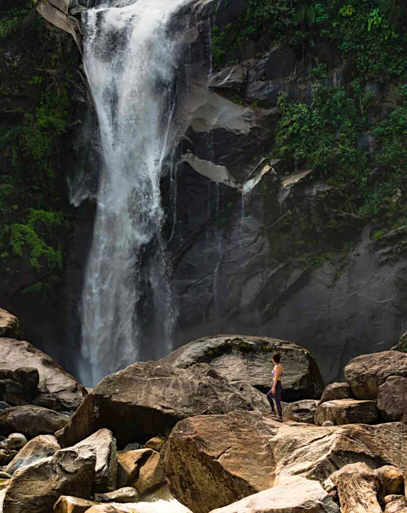 A woman stands in front of the Taparto Waterfalls near to Jardin in Colombia. The water drives down over the jagged rocks