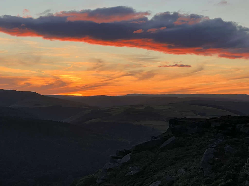 Sunset over the Peak District National Park, the sky glows orange and the land is in darkness