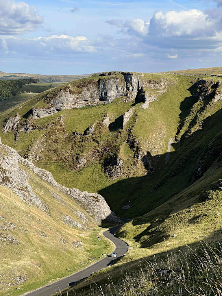 Looking east through Winnats Pass with the steep valley walls on either side under a cloudy blue sky