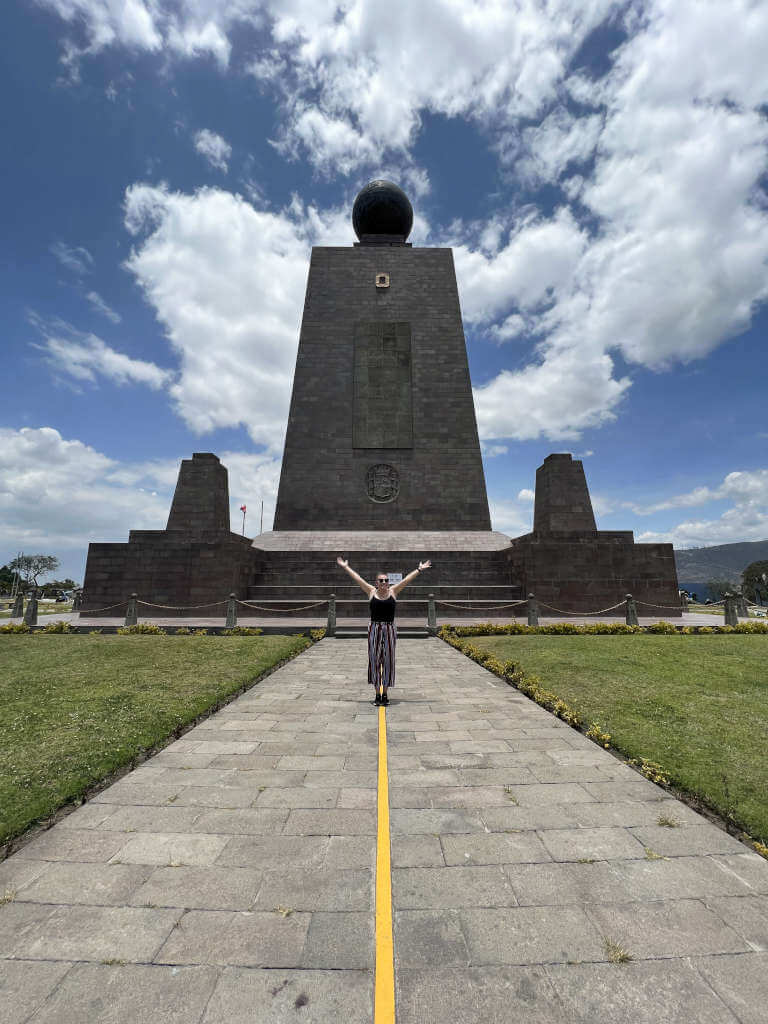 Zoe stood on the equator line at Mitad del Mundo with both arms in the air