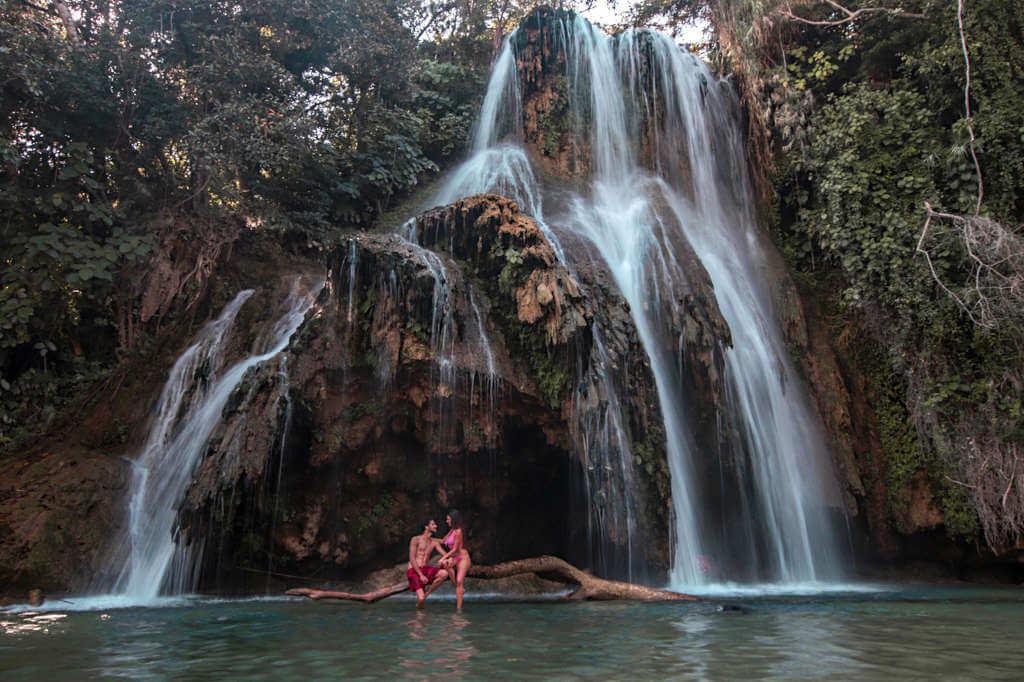 A couple sit on a branch in front of Tamasopo Falls in San Luis Potosi