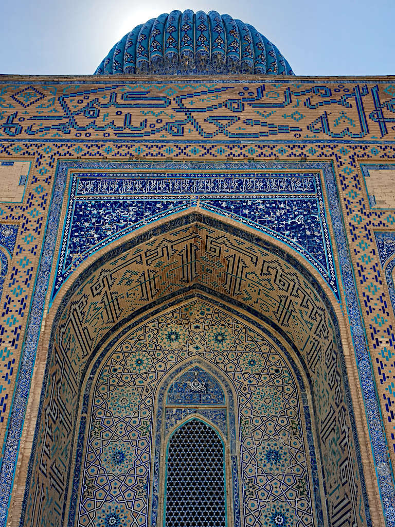 Intricately designed buildings in Turkistan with blue tiled patterns around the entrance and on the dome