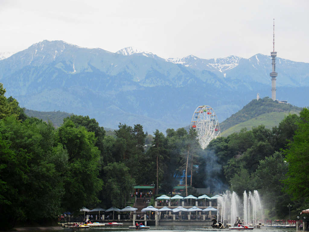 A ferris wheel and TV tower stand against a backdrop of snow-capped mountains in Almaty