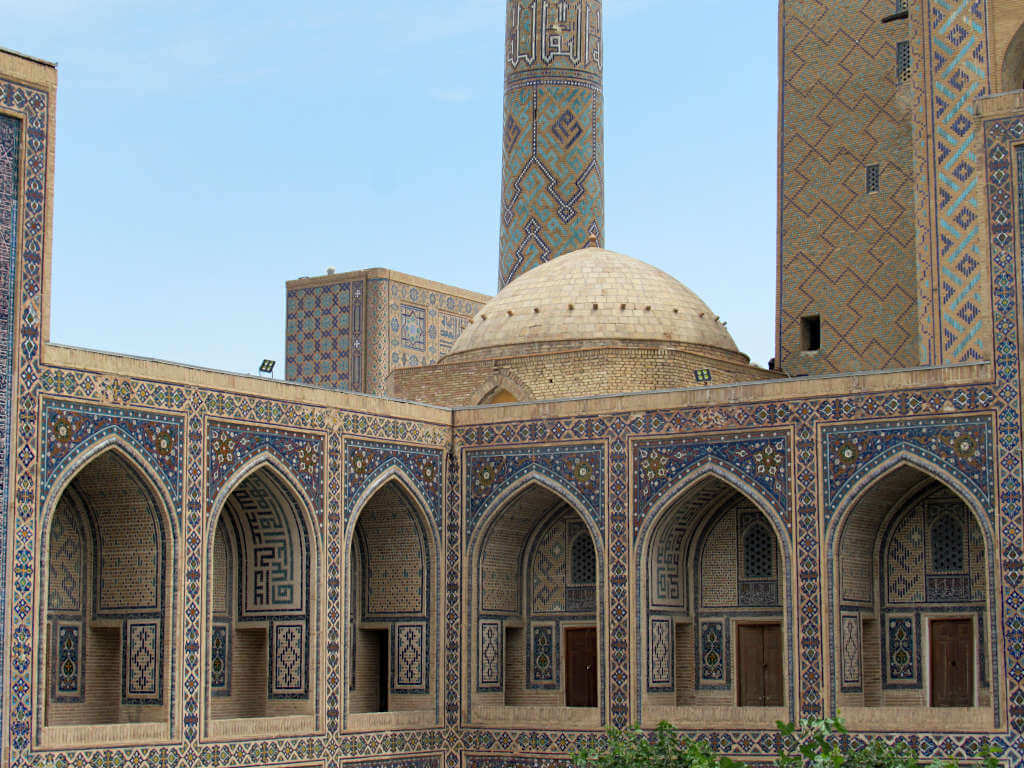 The best time to visit Uzbekistan is less important when there are beautiful buildings like this one standing all year round. Six archways under a dome and tower are photographed with blue patterned tiles all around.