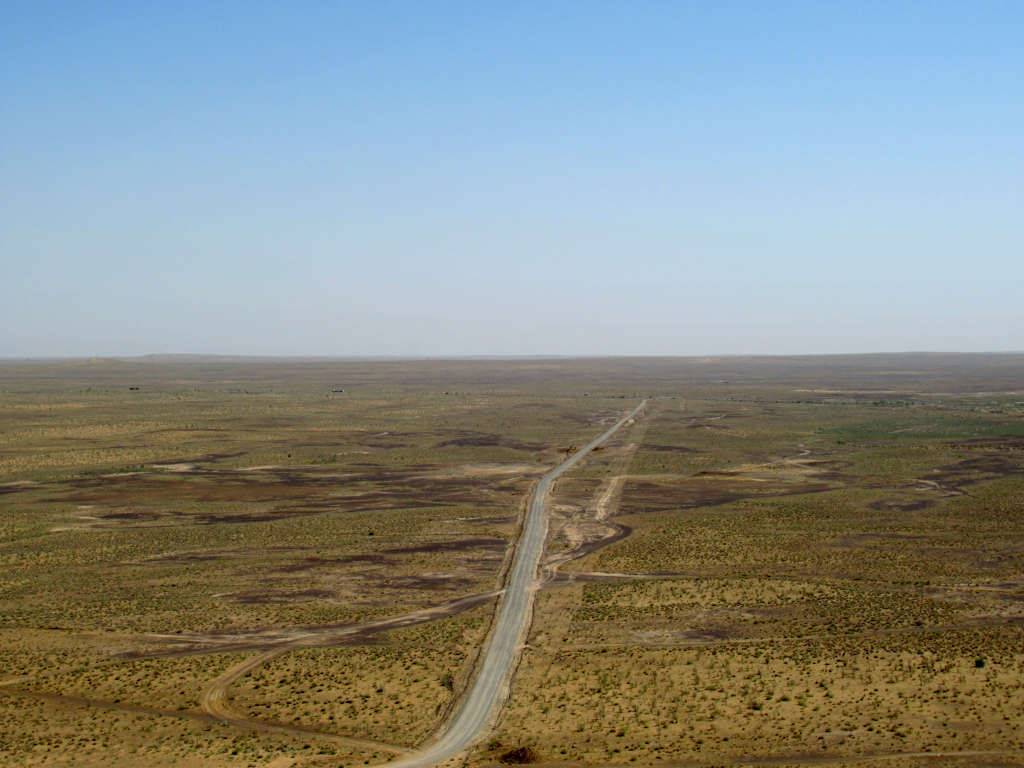 A long road cuts through the green-yellow fields with miles of flat land behind