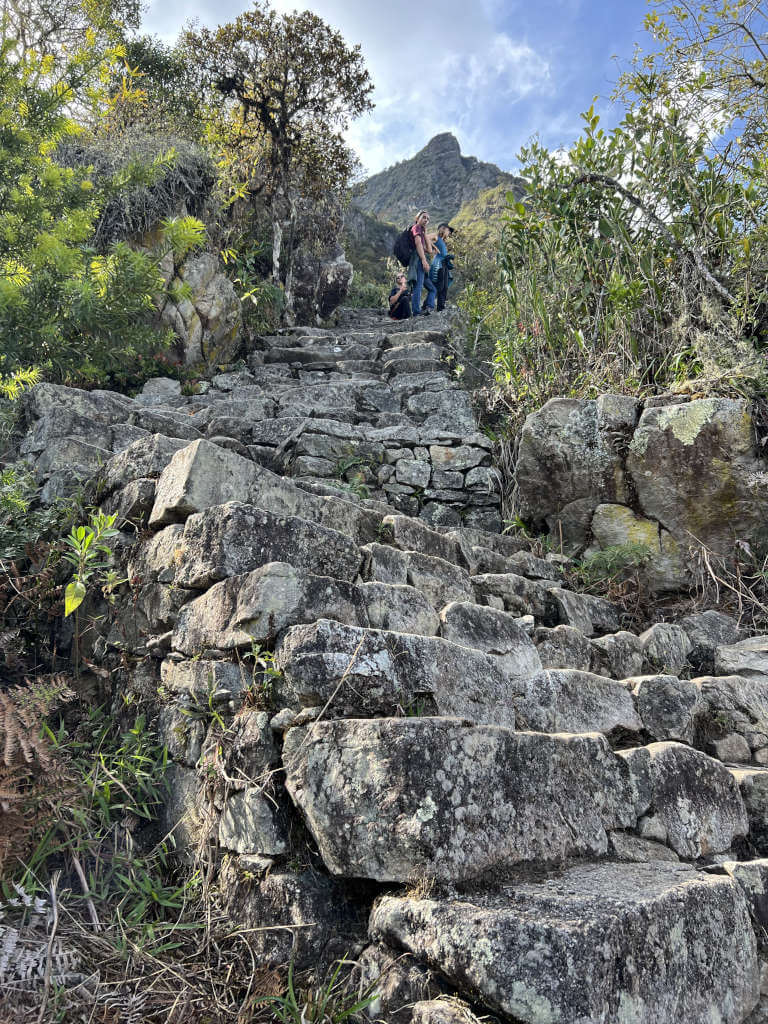 More steep stairs leading to the tall peak behind as three hikers take a rest on the steps