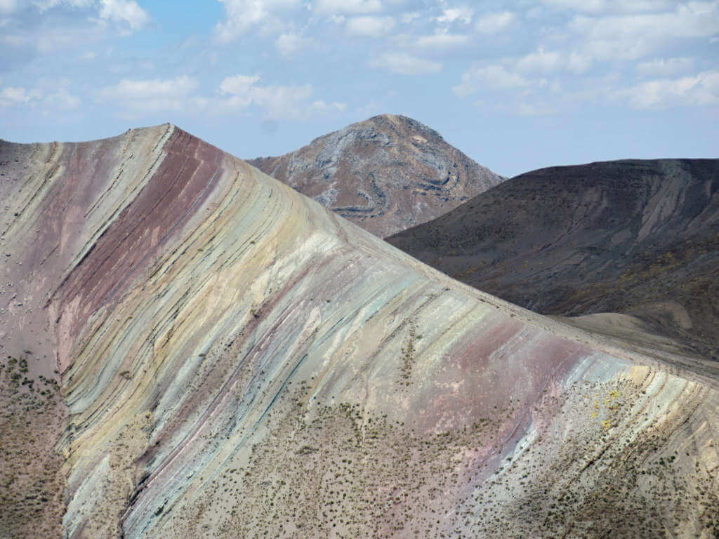 A close-up of the colours on Palcoyo Rainbow Mountain with other mountains in the background