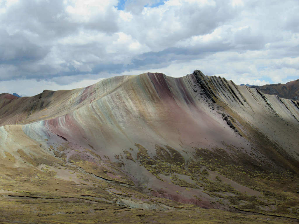 The ridge-topped mountain with various colours in stripes down each side against a cloudy backdrop