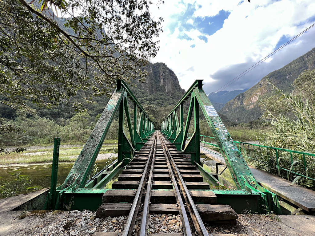 Looking along the train tracks across a green metal bridge - the path runs parallel along the right-hand side