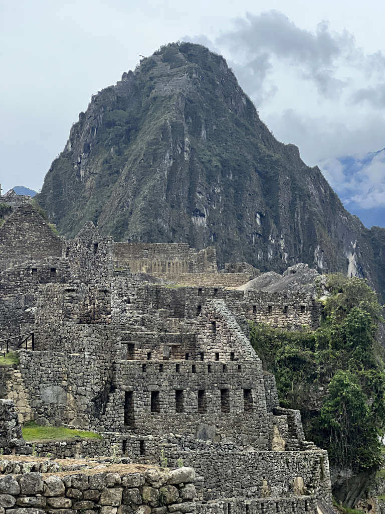 The impressive brick work of the ruins on the site with the imposing peak of Huayna Picchu behind against a cloudy background