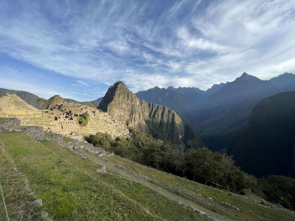 Machu Picchu at daybreak with a golden glow and light clouds.