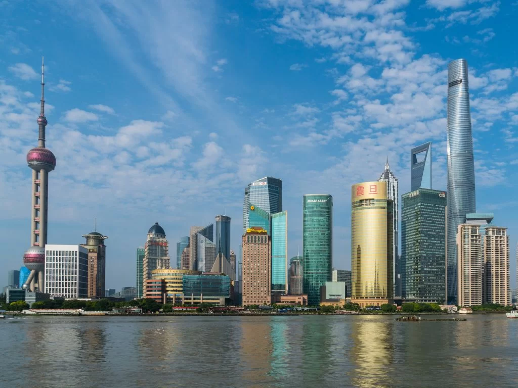 Looking at the skyscrapers of shanghai from the bund, with a blue sky behind and light, fluffy clouds