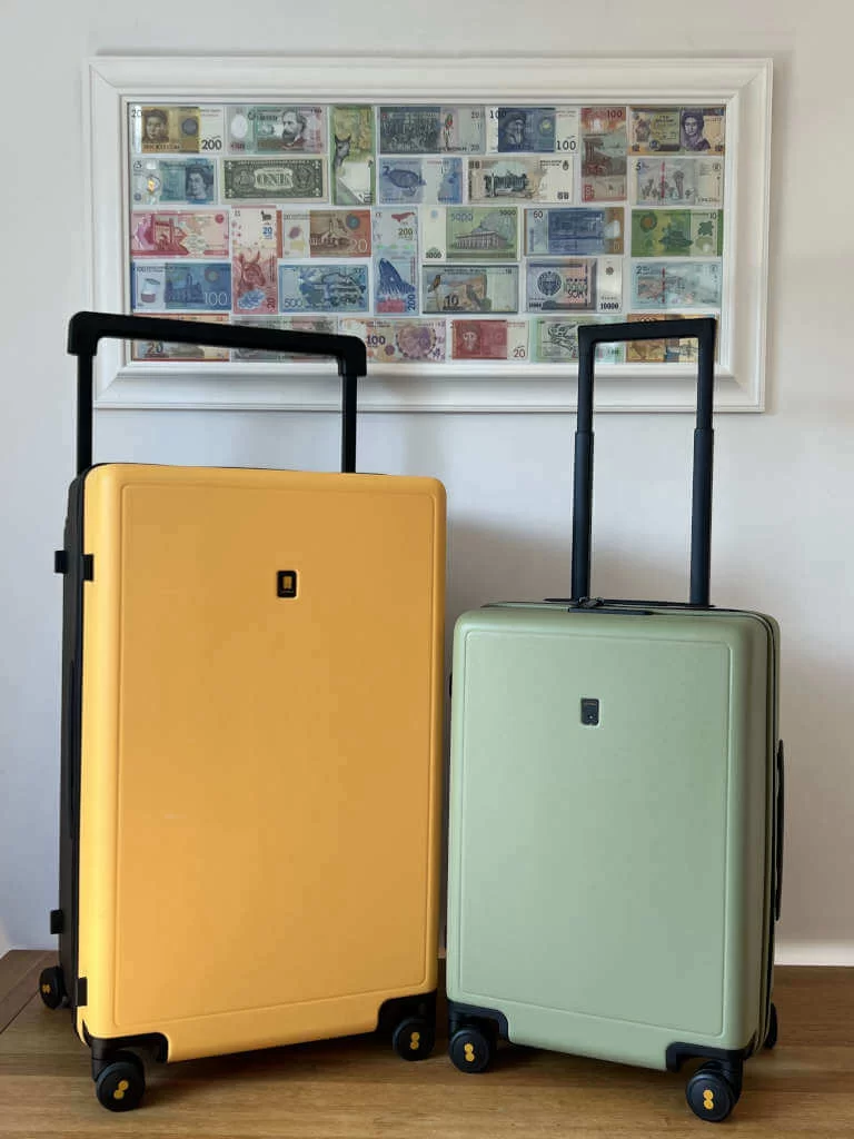 Two LEVEL8 suitcases pictured in front of a photo frame full of notes from different countries