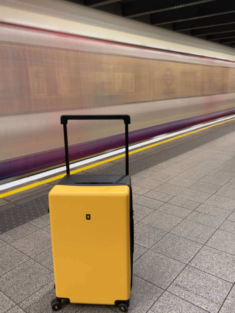 The LEVEL8 Voyageur 26 inch carry-on suitcase in front of a blurred tube train in London