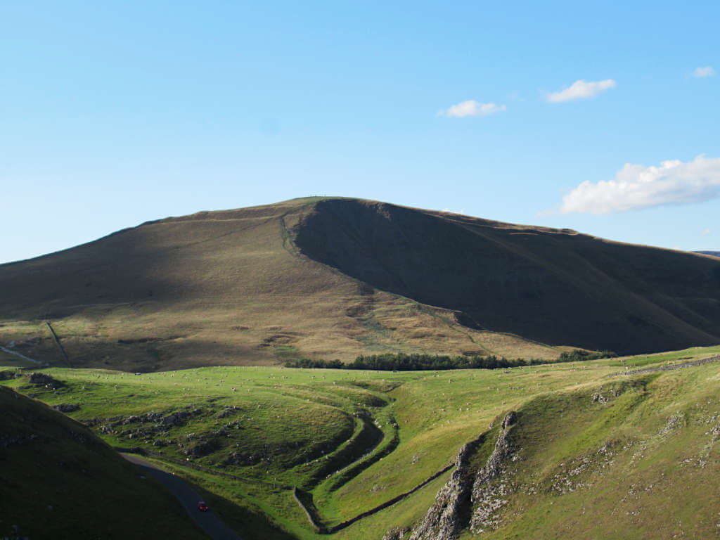 The imposing Mam Tor with its collapsed side against a blue sky with many sheep in the foreground