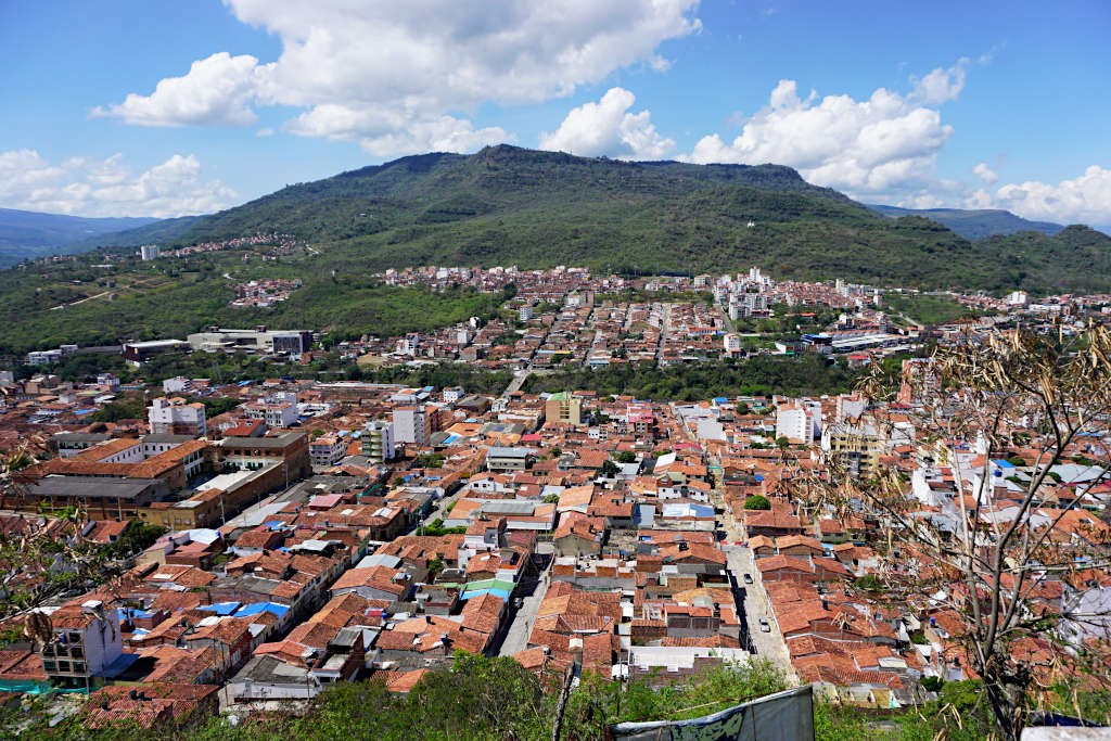 Looking over the small city of San Gil in the state of Santander in Colombia. Fluffy white clouds half cover the blue sky and a city full of orange roofs sits below.