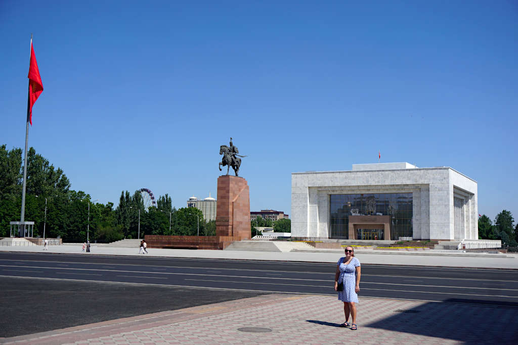 Zoe stood in front of the square with the flag visible on one side. The road behind her is completely empty and the sky is blue with no clouds