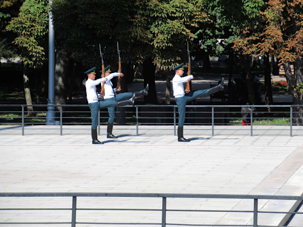 Three guards march away from their duty guarding the square. Their legs are at ninety degrees and they are carrying wooden guns in front of them